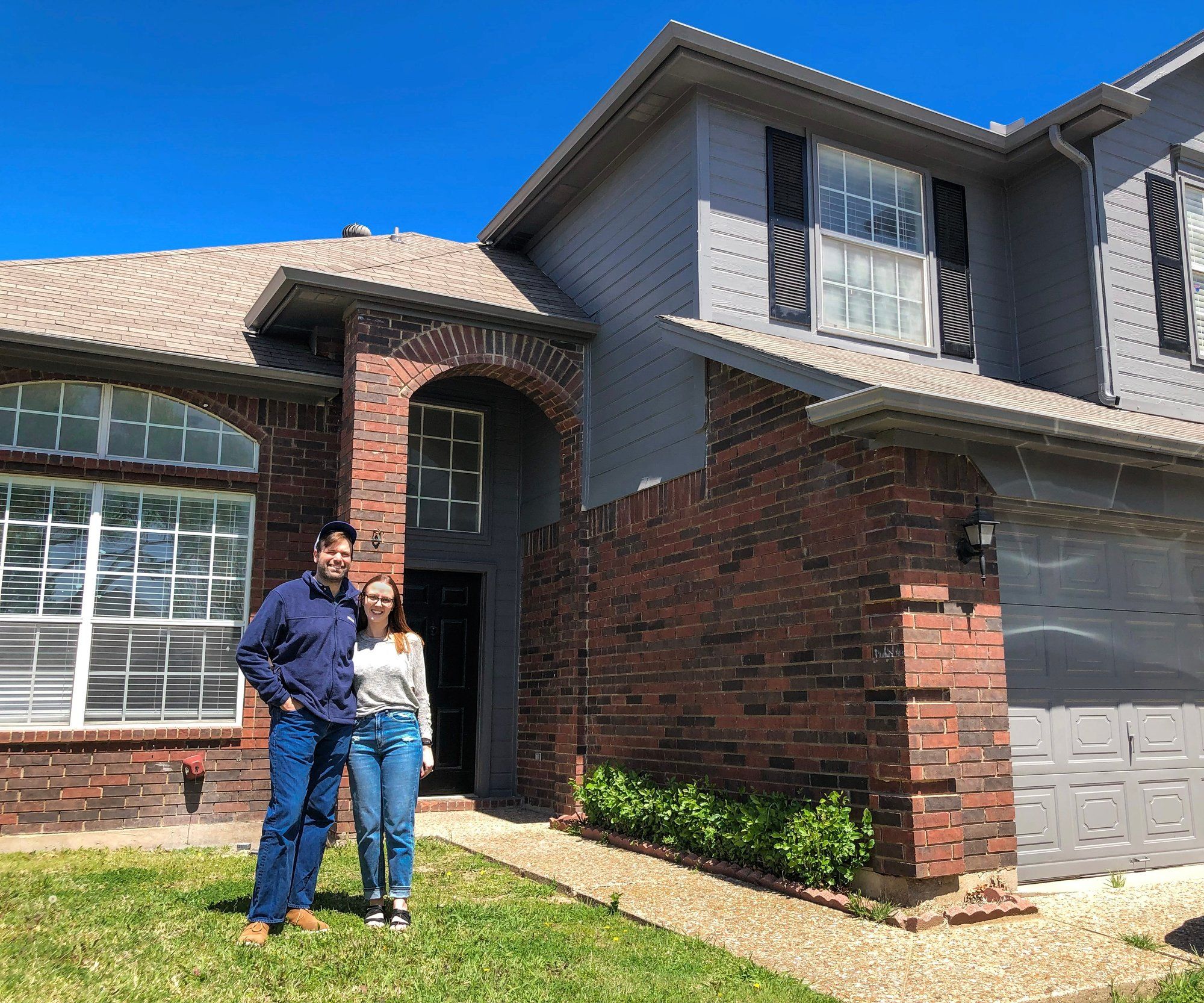 Leila and Dante stand on the lawn in front of a two-story brick house.